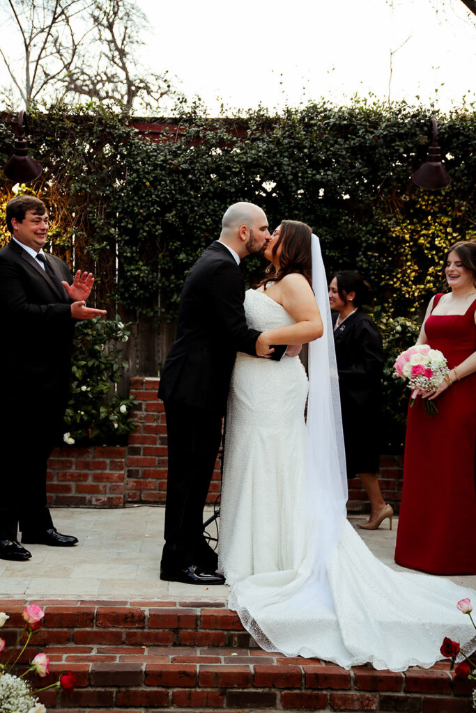 Bride and groom share their first kiss at the altar as guests and wedding party applaud.