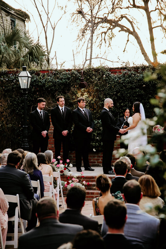 Bride and groom exchange vows in an intimate outdoor courtyard ceremony surrounded by family and friends.