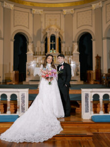 Newlyweds pose at the altar inside Our Lady of the Gulf Catholic Church with the bride's long lace train spread across the wooden floor.