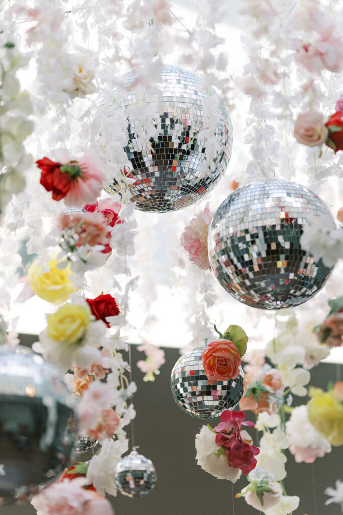 Silver disco balls hang among cascading white blossoms and colorful flowers as part of the reception décor.