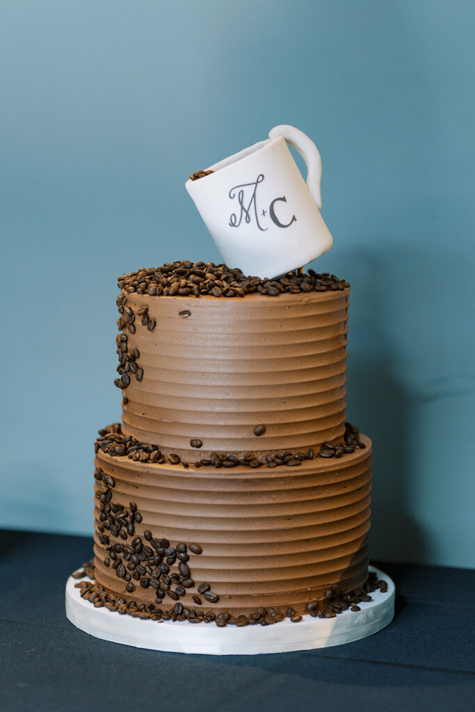 Two-tier chocolate wedding cake decorated with coffee beans and topped with a monogrammed coffee mug.