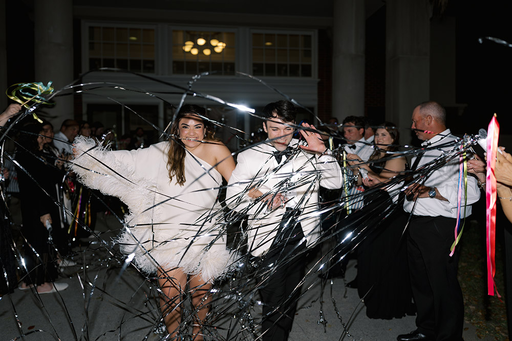 The newlyweds run through a ribbon streamer exit at the end of their reception, smiling as guests celebrate around them.