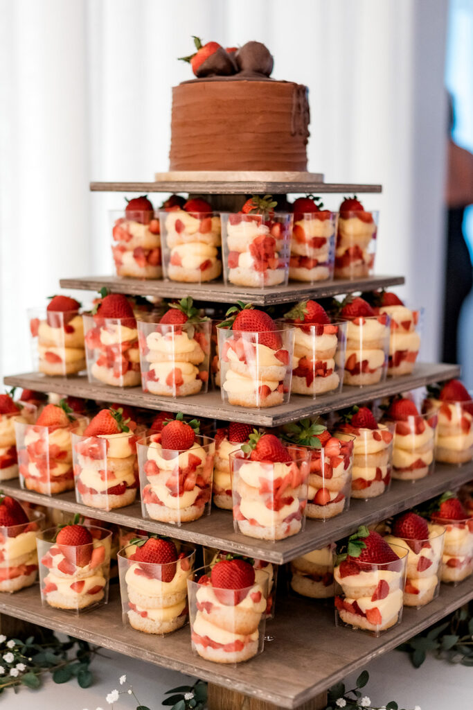 Tiered dessert display featuring chocolate-covered strawberries and individual strawberry shortcake parfaits arranged on rustic wooden shelves.