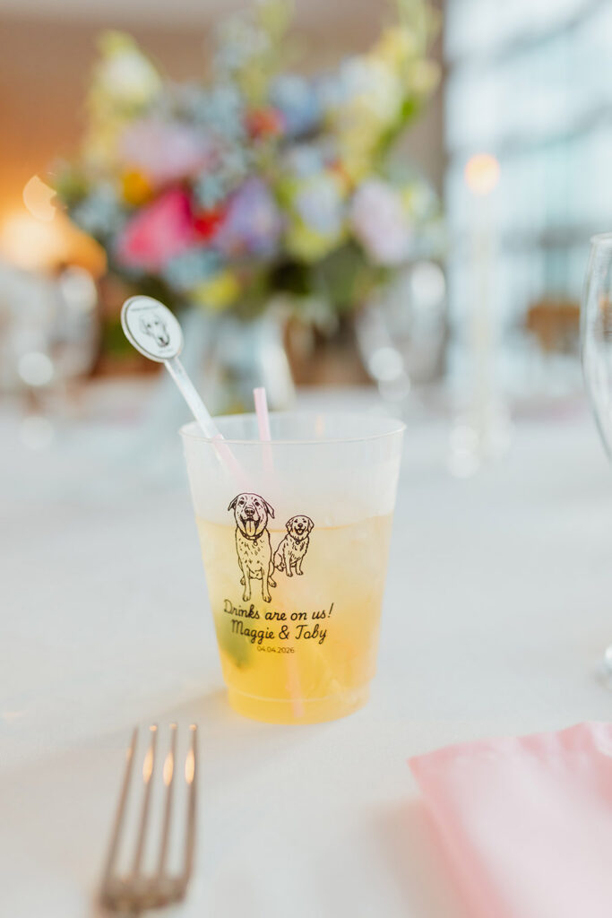 A signature wedding cocktail in a custom cup featuring the couple's dogs sits on a reception table.