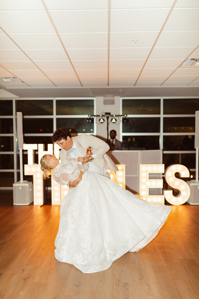 The couple shares a dramatic dip during their first dance in front of illuminated marquee letters.