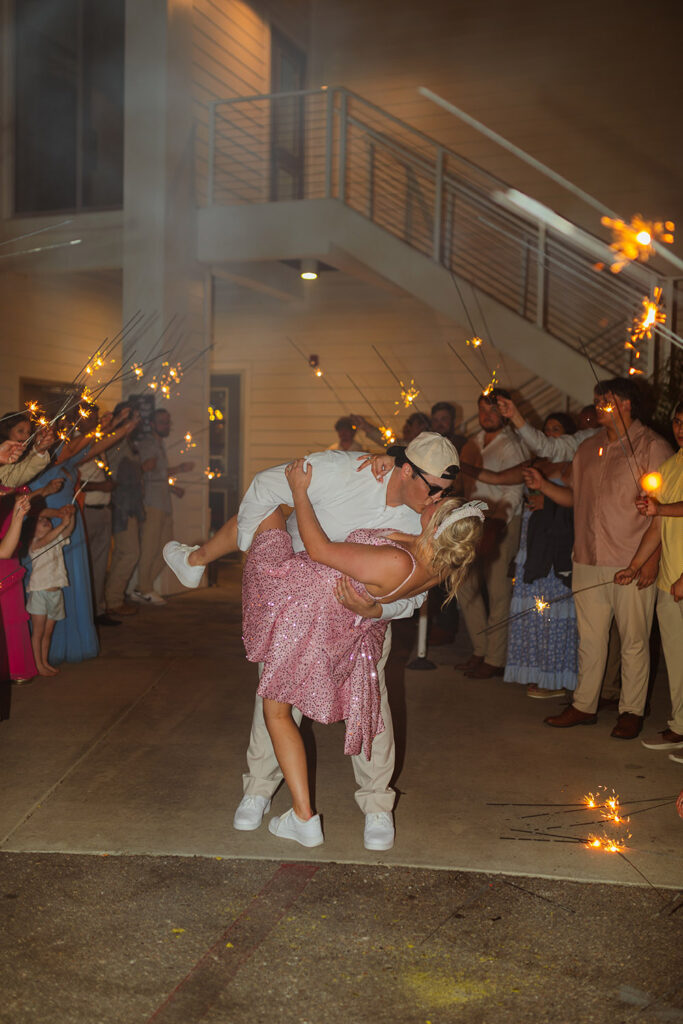 The couple shares a kiss during a sparkler send-off as guests line the walkway with sparklers.