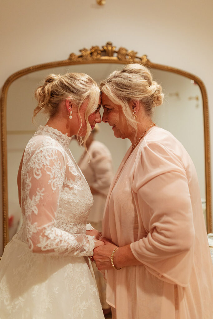 The bride shares an emotional forehead-to-forehead moment with her mother while getting ready.