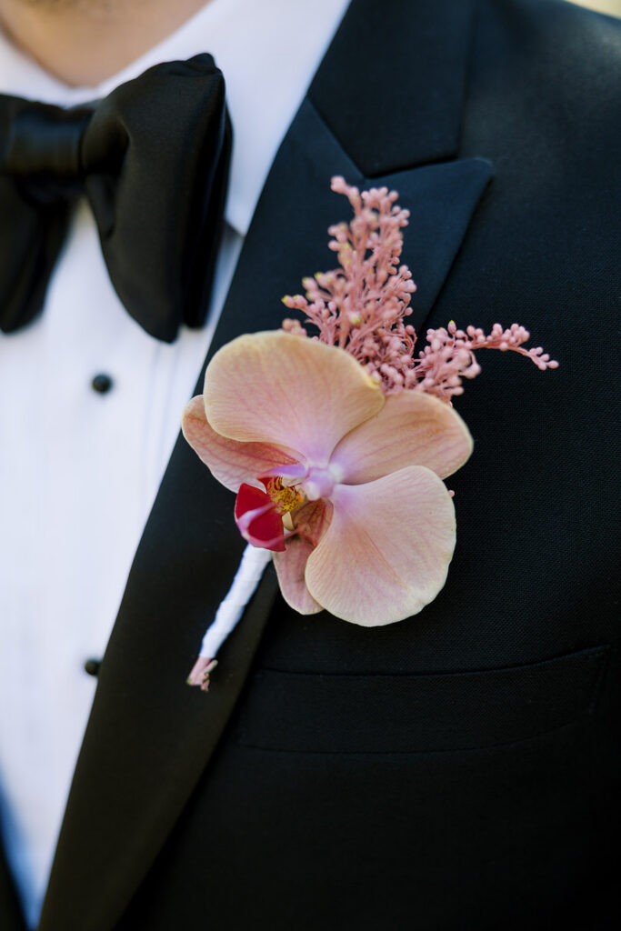 Close-up of the groom's blush orchid boutonniere accented with pink astilbe on a classic black tuxedo.