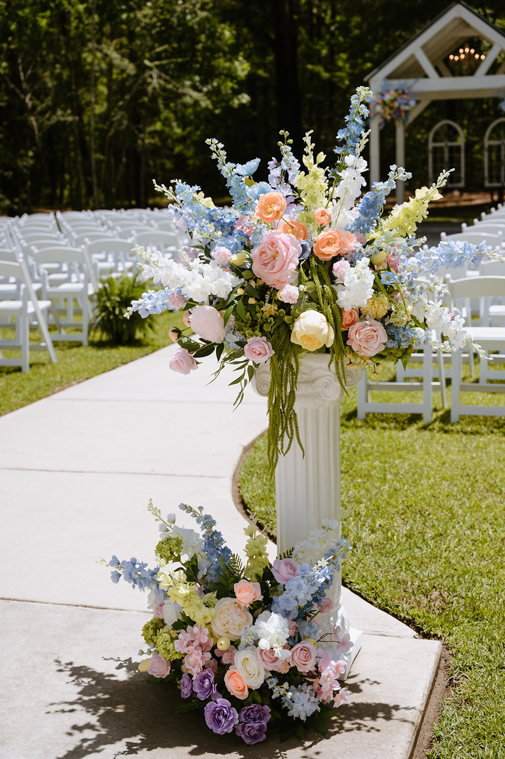Colorful pastel floral arrangement on a white pedestal lining the outdoor ceremony aisle.