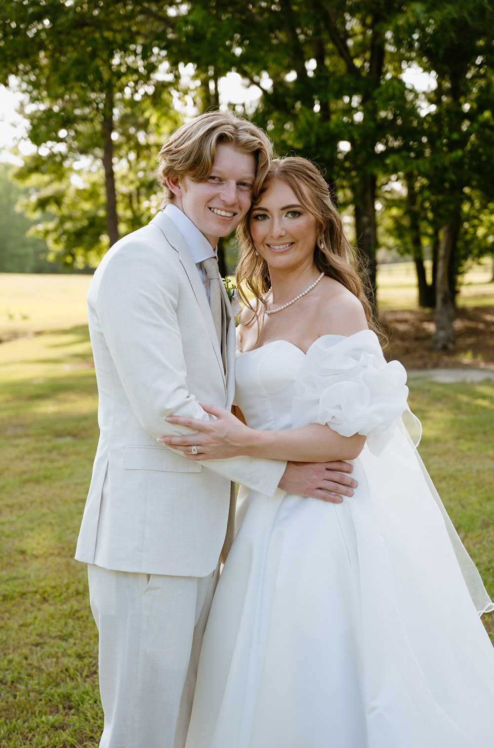 Bride and groom embrace outdoors, smiling at the camera after their ceremony.
