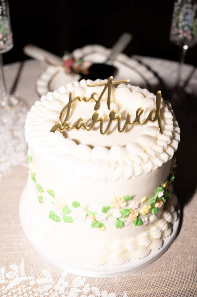 Small white frosted wedding cake with vintage piping and a gold "just married" topper.