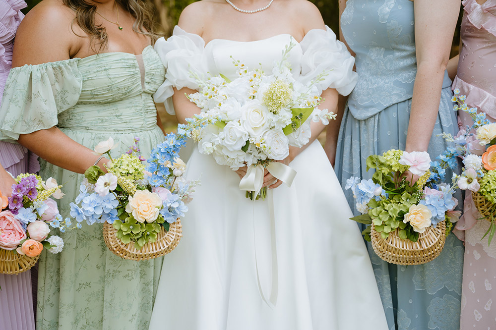 Close-up of the bride's white bouquet surrounded by bridesmaids holding colorful basket floral arrangements.