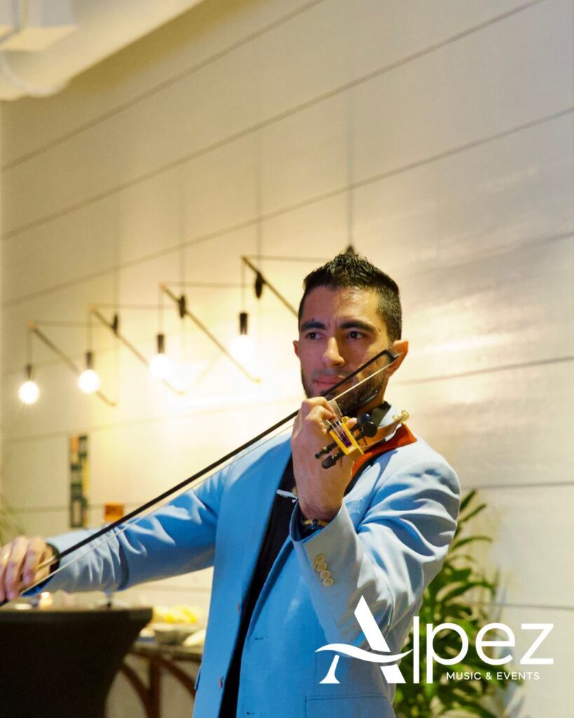 Man in light blue suit plays violin indoors with modern lights, plants, and Alpez Music & Events logo in corner.
