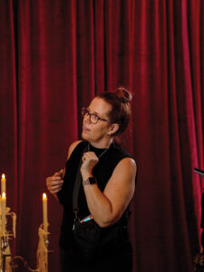 NOW Weddings Magazine Jessica Burke makes final adjustments to the editorial set while standing in front of burgundy drapery and candlelight.