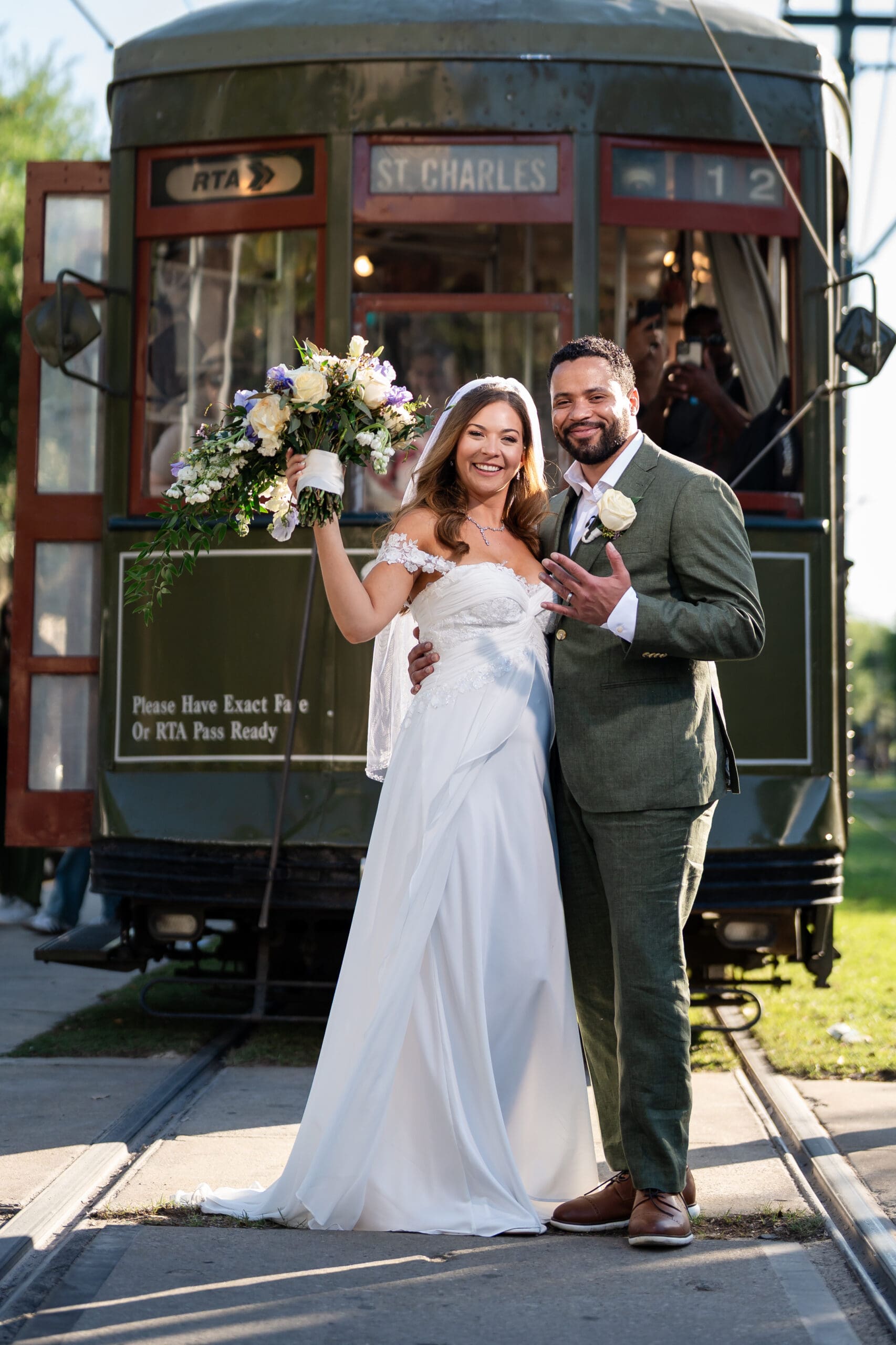 Happy bride and groom pose by a green St. Charles streetcar, celebrating their Louisiana wedding with a large bouquet.
