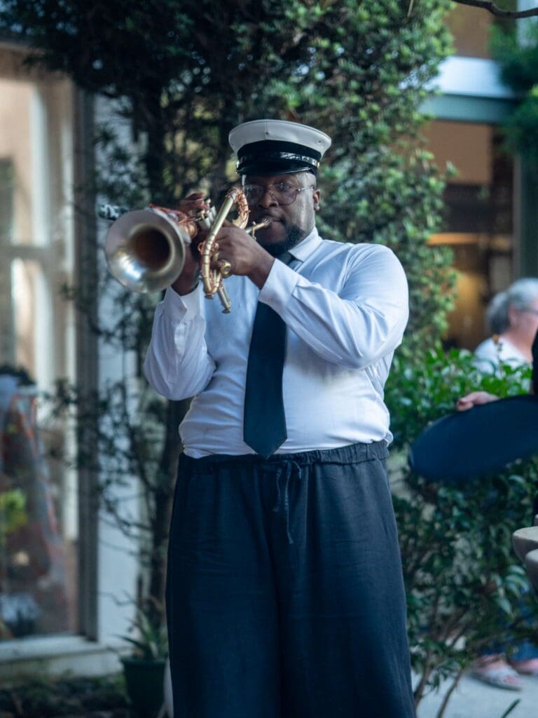Man in uniform cap, white shirt, and tie playing a trumpet.