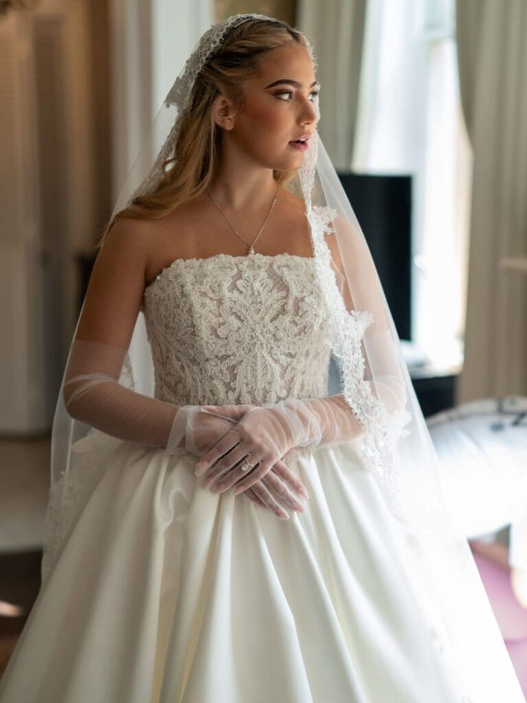 Bride in a strapless lace gown, sheer gloves, and a veil looking to the side.