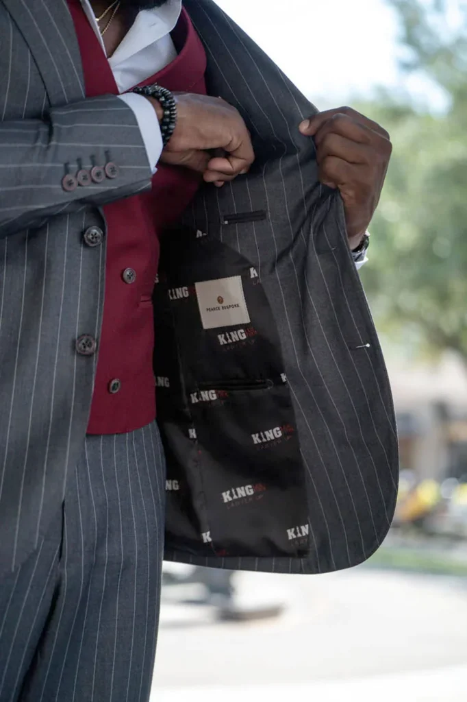 A man in a grey pinstripe suit and burgundy vest revealing the branded lining by Pearce Bespoke.