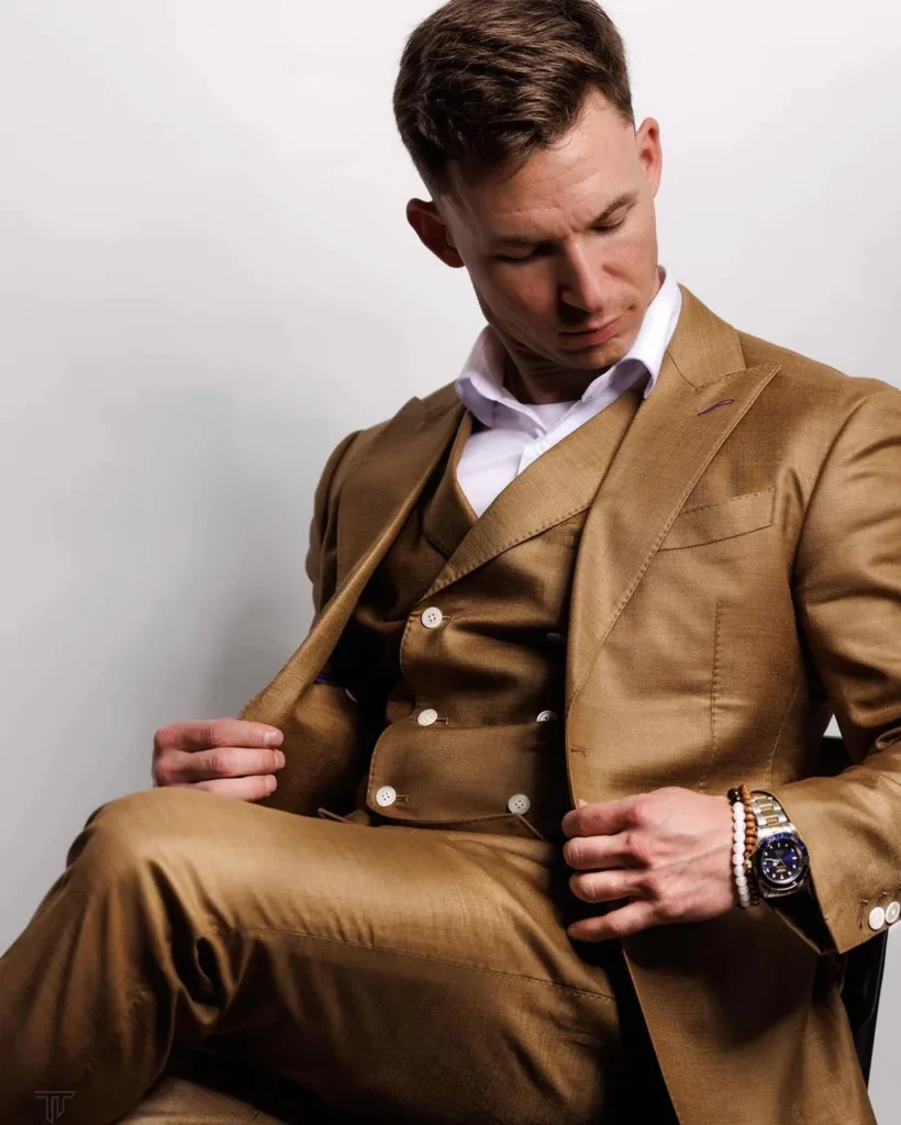 A man in a tan three-piece suit adjusting his jacket for a content creation shoot.