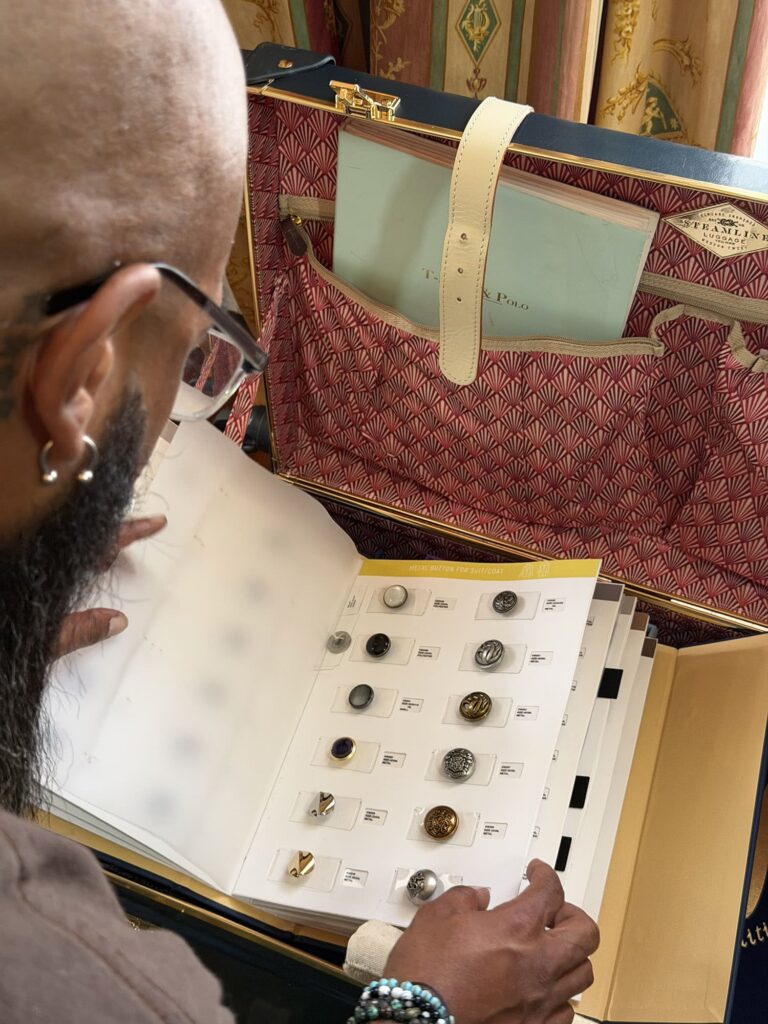Johnny Lee of Pearce bespoke browses a display book of suit jacket buttons inside an open trunk.