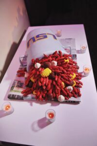 LSU mug spills crawfish, corn, and potatoes onto newspaper-covered table with votive candles.