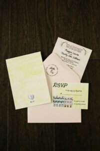 Wedding invitation set with cream envelope, illustrated cards, and RSVP on dark wood background.