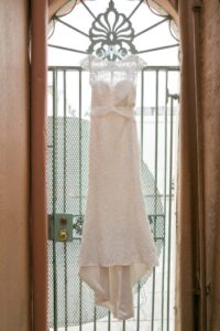 White lace wedding dress hangs on an ornate metal gate beneath an arched doorway.