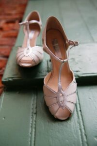 Light-colored T-strap high heels sit one in front of the other on green wooden steps.