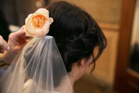 Person with dark braided hair, white veil, and peach flower, seen from behind.