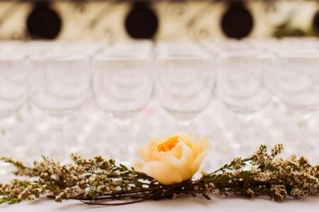 Yellow rose with greenery on a table, wine glasses blurred in the background, hinting at an elegant event.