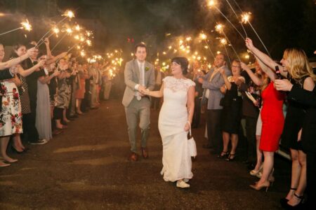 Bride and groom walk happily through guests with sparklers at night, celebrating their wedding with cheers and smiles.