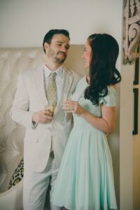 Smiling man in a light suit and woman in a mint dress hold champagne glasses at a formal event.