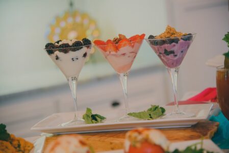 Layered yogurt parfaits in martini glasses topped with berries, granola, and mint on a white plate on a kitchen countertop.