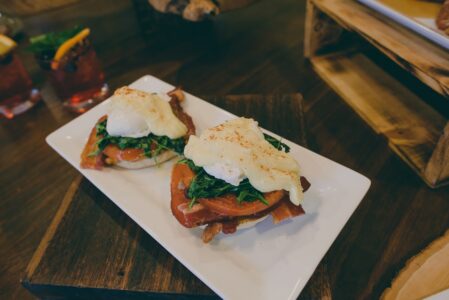 Eggs Benedict with spinach and hollandaise on a white plate, garnished with paprika, served on a dark wood table.