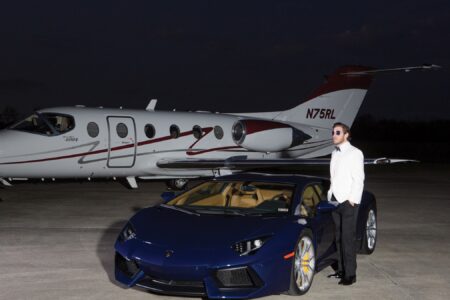Man in white jacket by blue Lamborghini on airstrip at night, private jet in background.