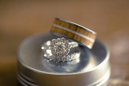 Wooden inlay ring on a round surface beside diamond engagement and wedding rings, sparkling in warm light.