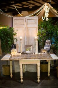Rustic wedding table with candles, framed photos, and Mr & Mrs signs, set by wooden panels, greenery, and string lights.