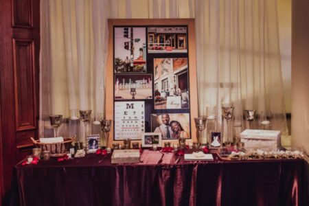 Table with framed photos, candles, trinkets, a collage of wedding and city images, deep purple cloth, and rose petals.