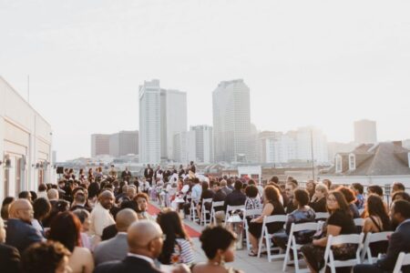 People seated on white chairs at a rooftop event at sunset, with tall city buildings in the background.