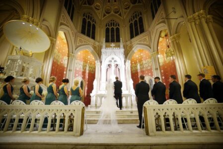 Bride and groom at altar in grand church, flanked by bridesmaids in green and groomsmen in black.
