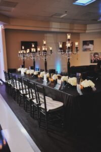 Elegant dining table with black chairs, candelabras, glass candle holders, and white flowers in a softly lit room.