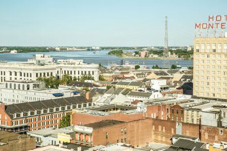 Aerial view of New Orleans buildings, Mississippi River in the background, and HOTEL MONTE sign visible on a tall hotel.