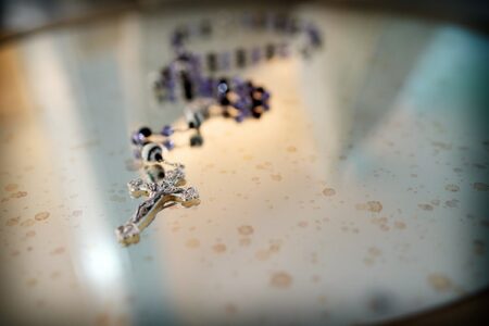 Silver rosary with crucifix on reflective surface, focused crucifix and blurred beads—elegant wedding or Louisiana detail.