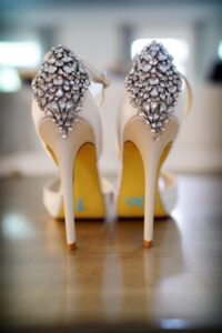 White high heels with sparkling rhinestone heels on a wooden surface, ideal for Louisiana wedding inspiration.