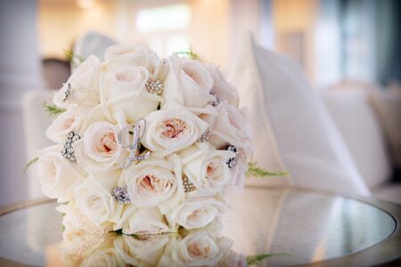 Pale pink and white rose bouquet with jewels on glass table, elegant Gulf South wedding inspiration, soft warm background.