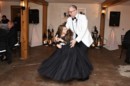 A man in a white tux dances with a smiling girl in black at a warmly lit Louisiana wedding with candles and lanterns.