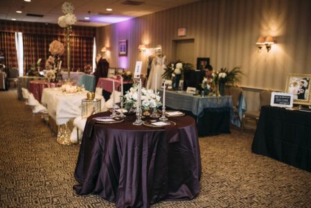 Elegant banquet room with dark-covered round tables, floral centerpieces, and themed displays throughout.