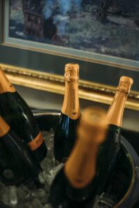 Sparkling wine bottles with gold foil tops chill in an ice bucket, framed painting in the background.