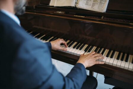Hands and upper body of a suited person playing piano with sheet music on the stand.