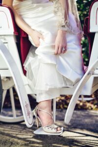 Bride in white dress and lace heels steps out of a white carriage, lifting her skirt with one hand.